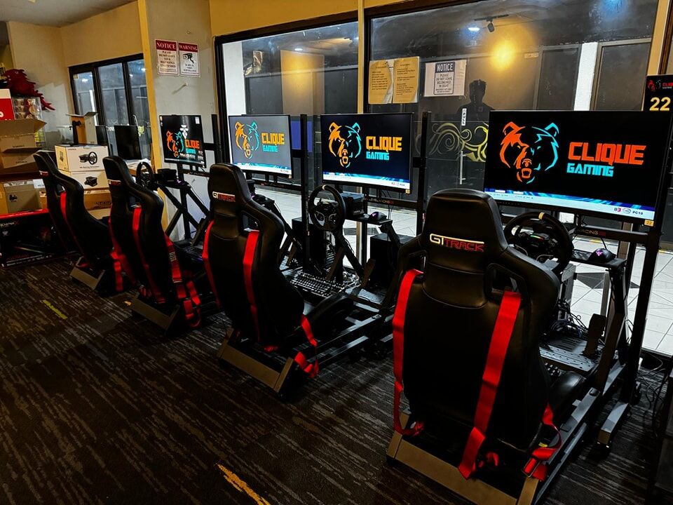 image shows row of black and red gaming chairs at table with row of pc gaming computers in Clique Gaming esports cafe.